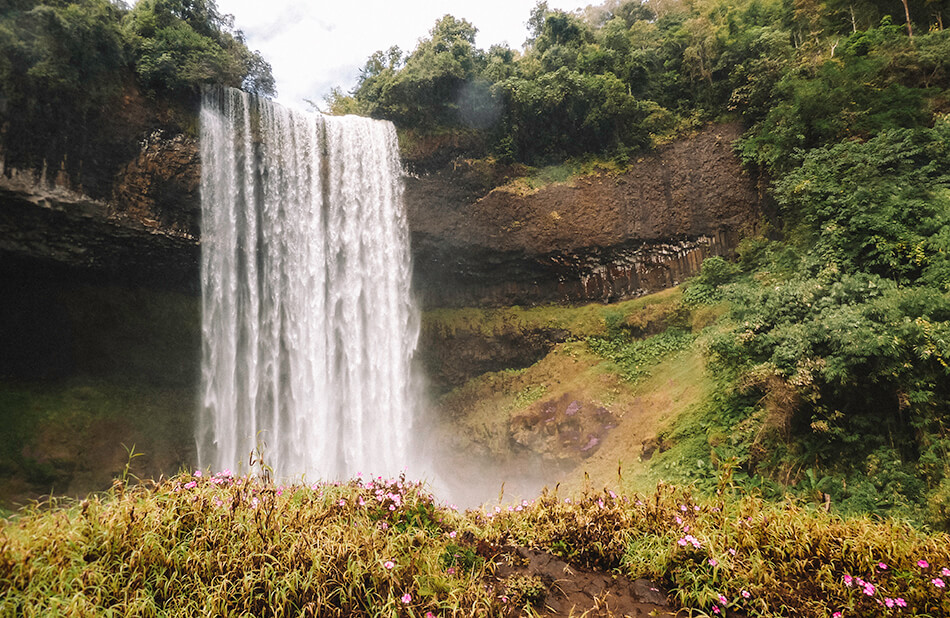 Hiking down a slippery path to the base of Tad Tayicsua Falls while driving the Bolaven Plateau Big Loop