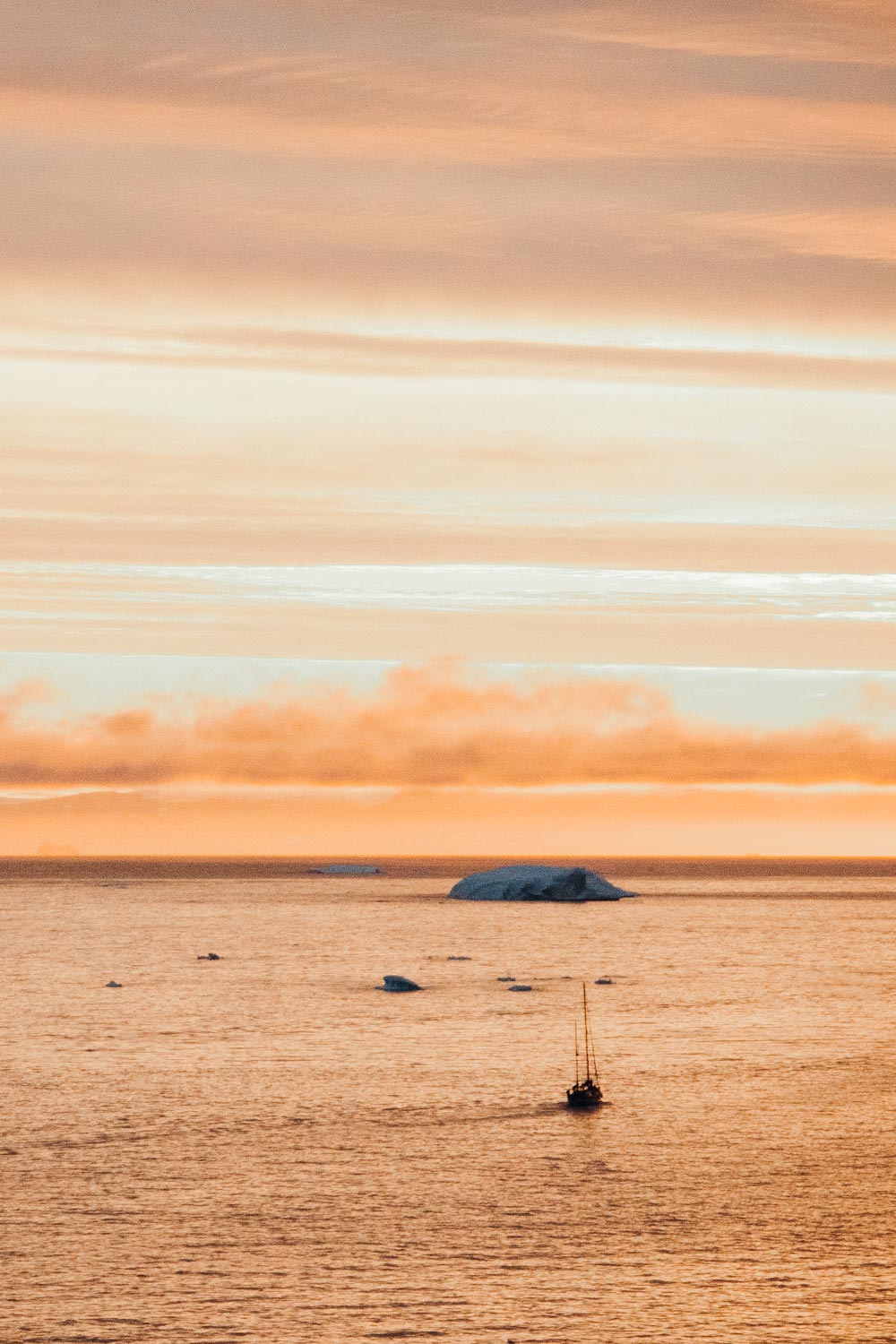 Sunset hues cast a warm glow on the icebergs during a midnight sun cruise